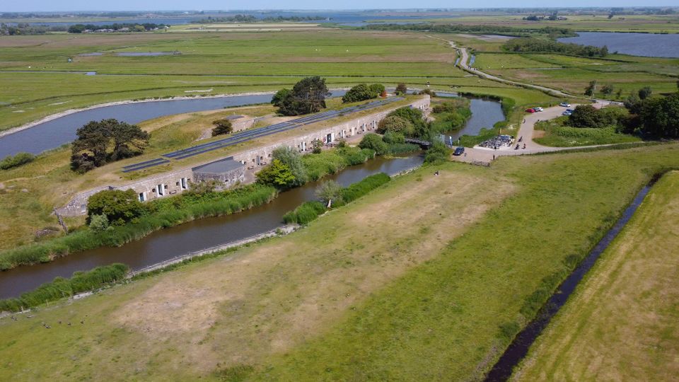 Een betonnen fort overgroeid met gras, gefotografeerd vanuit de lucht.