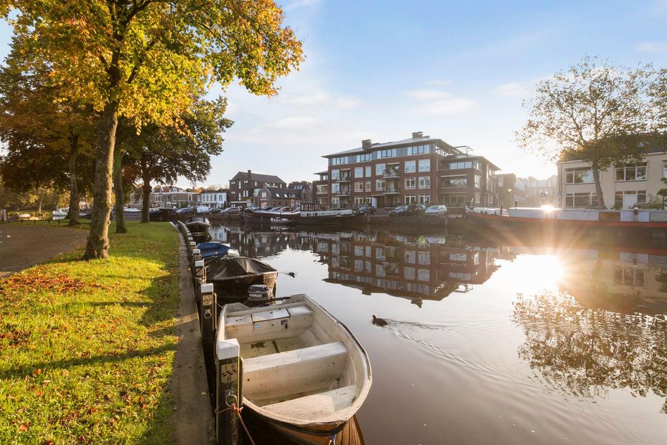 Stadskade Emmakade in Woerden, Groene Hart, met aangemeerde bootjes langs het water, bebouwing aan de overzijde en bomen in herfstkleuren bij laagstaande zon.