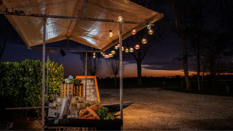 Sfeervol verlichte kraam met stamppotten en groenten bij zonsondergang tijdens de drive-through bij Kameryck.