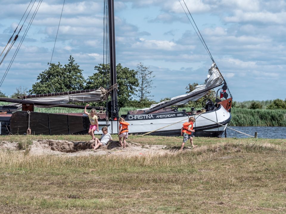 kinderen spelen in het zand met op de achtergrond een boot