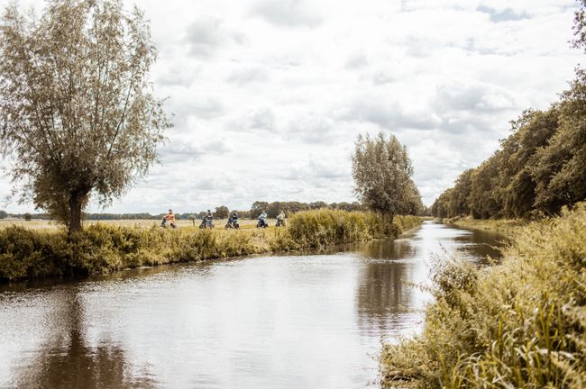 Groep fietsers rijdt door het landelijke buitengebied van Woudenberg langs een brede watergang. De foto laat fietsen door het open landschap en de groene omgeving van de Grebbelinie zien.