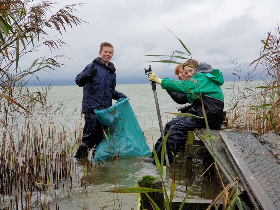 2 jongens in het water met vuilniszakken in de hand.