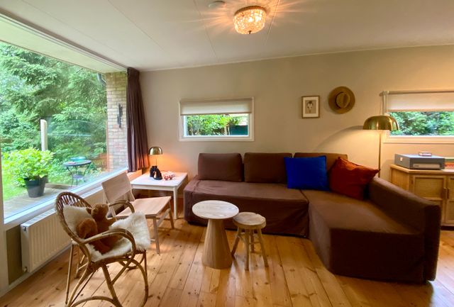 De woonkamer van Boshuisje Wateren I is knus ingericht en vanaf de bank kijk je zo de tuin in door de grote ramen en kun je de vogels en eekhoorns goed volgen.