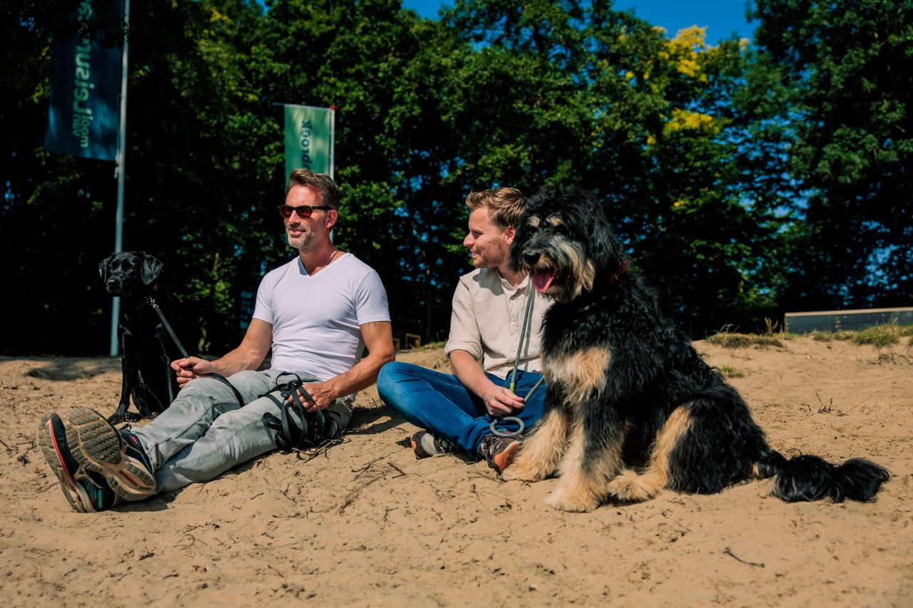 Mannen zitten op het strand met hun hond.
