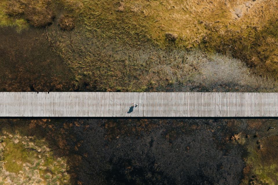 Drone foto van een man die wandelt over een langgerekt plankenpad in natuurgebied Hart van Drenthe op een zonnige dag.