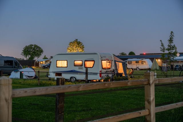 Avondfoto van diverse caravans met verlichting aan achter een hek.
