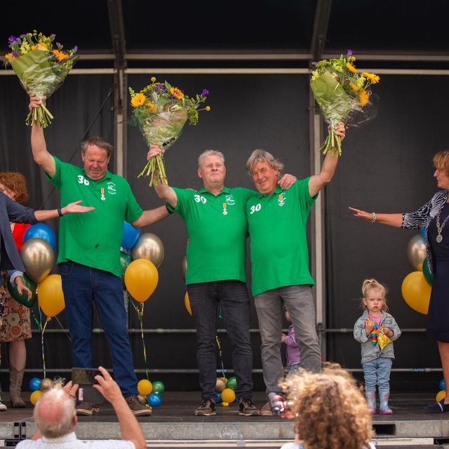 Drie manen met groene polo's die op het podium bloemen ontvangen omdat het vrijwilligers waren bij de Trekkertrek.