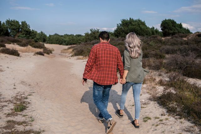 Een man en vrouw lopen hand in hand door het zand over de hei.