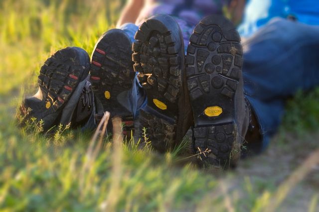 Zwei Paar Wanderschuhe und die Beine von Wanderern, die im Gras sitzen.