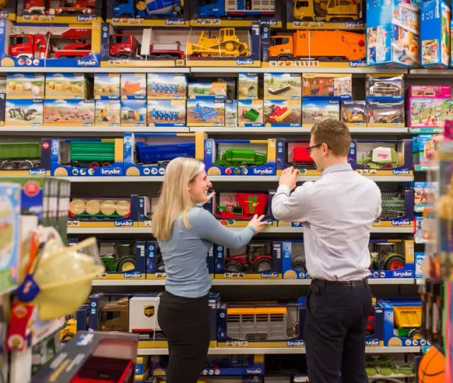 Twee mensen voor een winkelschap vol met speelgoed bij Sikma's Warenhuis in Bolsward.