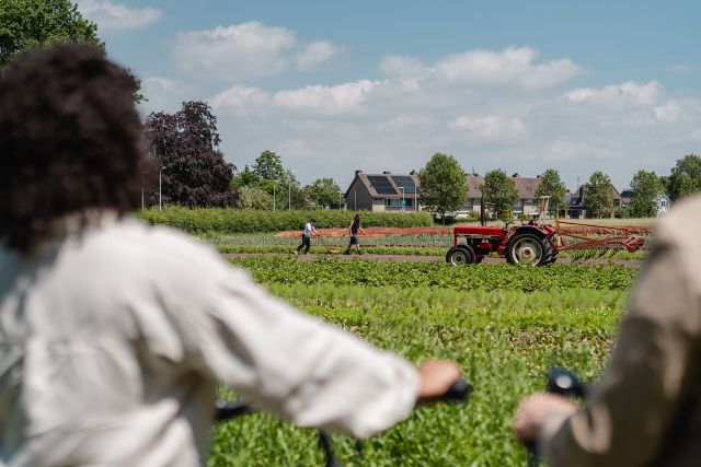 Foto van twee fietsers die uitkijken over een akker met een tractor en een boer.