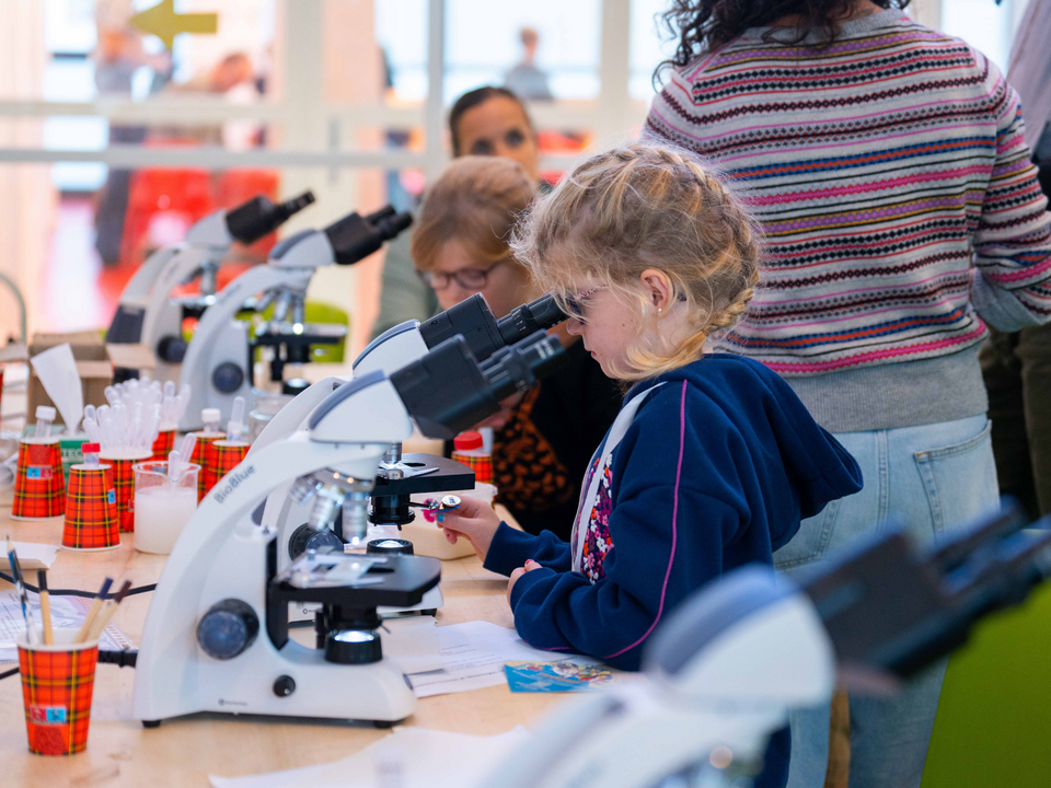 Meisje tijdens Science Day kijkend in een microscoop