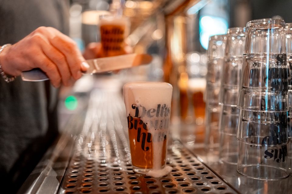 Een glas bier waarvan het schuim eraf wordt gehaald in Delfts Brouwhuis