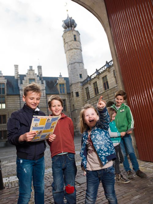 Een groepje kinderen doet de stadsstenen speurtocht en staat onder de poort van het Markiezenhof.