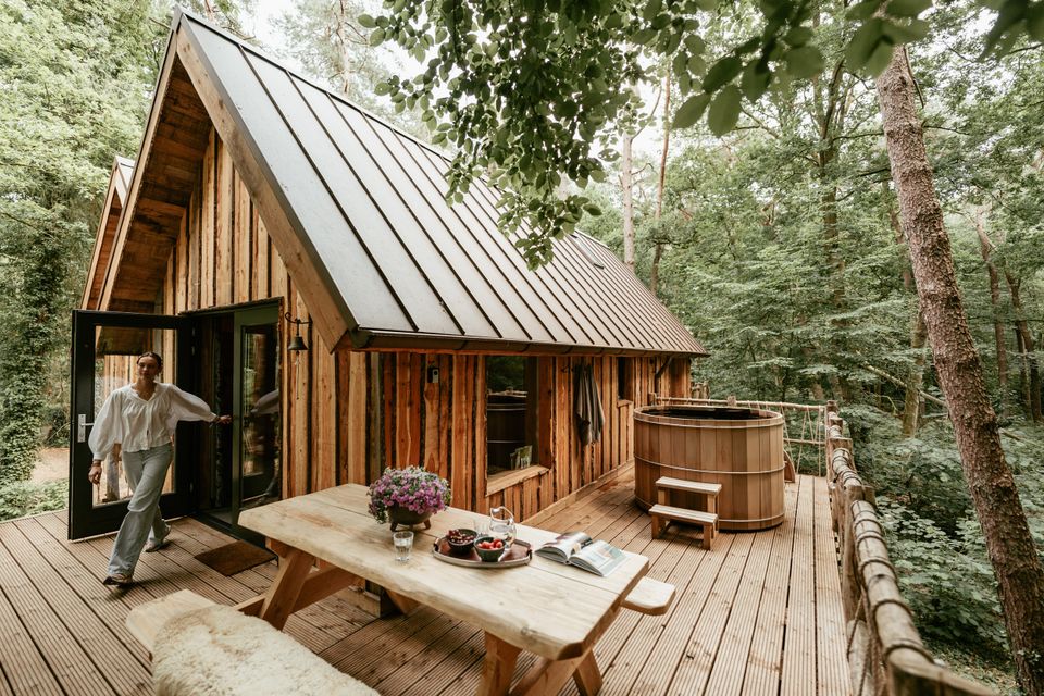 Houten boomhuis met terras, picknickset en hottub en vrouw die naar buiten komt