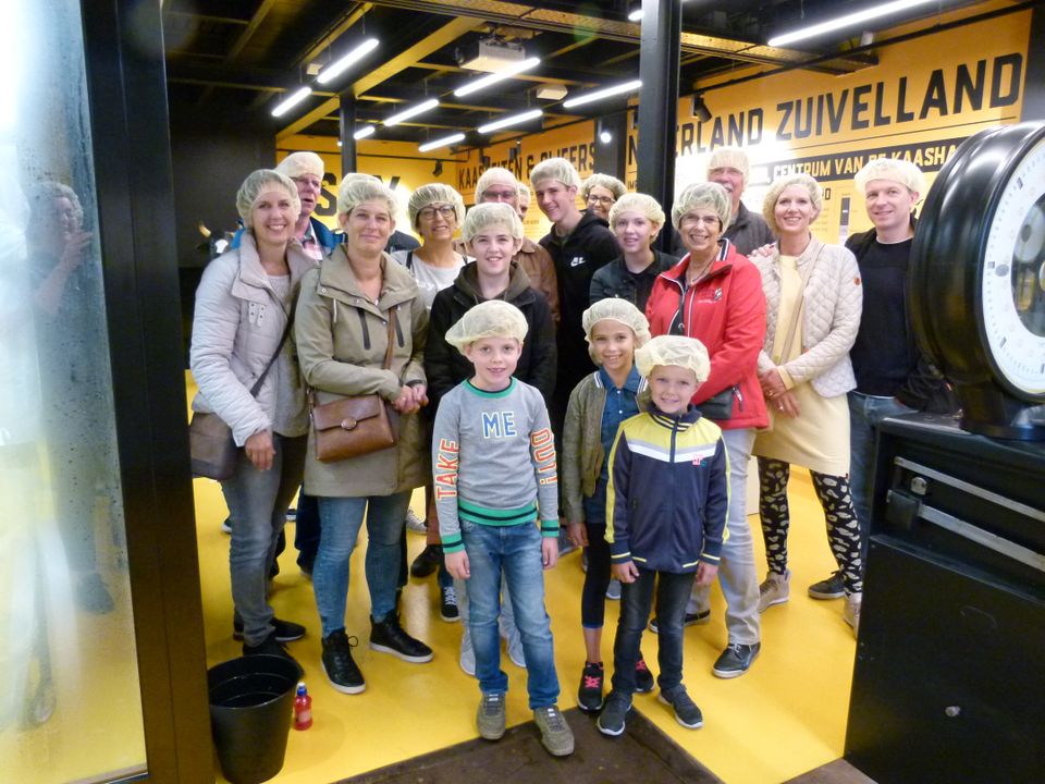 Kaasbeleving in het Kaaspakhuis in Woerden, Groene Hart, met een groep volwassenen en kinderen met haarnetjes tijdens een activiteit rond kaas maken.