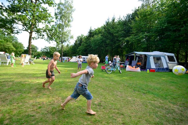 Kinderen spelen voetbal op het grasveld van Allurepark De Zeven Linden in Baarn, tussen caravans en kampeerplaatsen. De foto laat de kindvriendelijke en actieve sfeer op de camping zien.