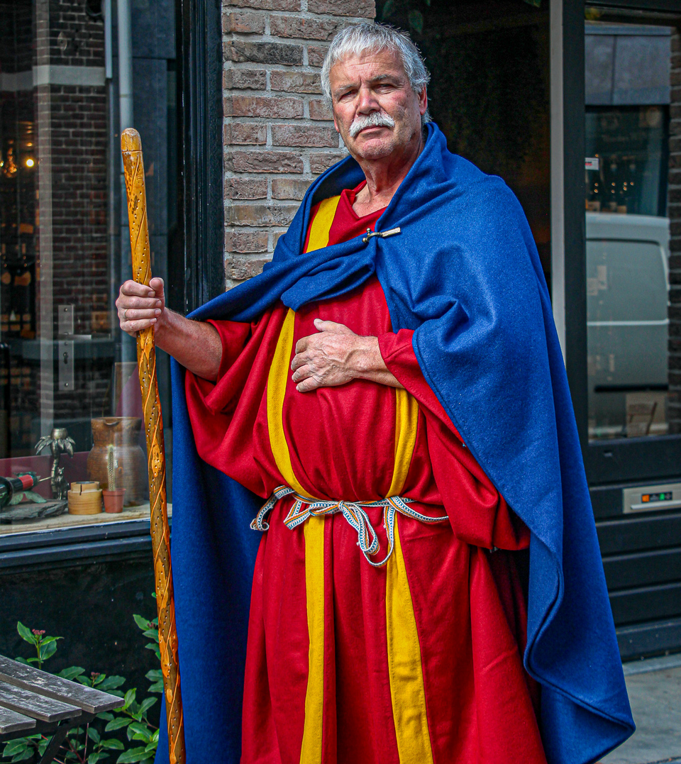 Historische Romeinse re-enactor Lucius Terentius Bassus in Woerden, Groene Hart, tijdens een Romeinenwandeling of audiotour. Persoon in Romeinse kleding met staf en blauwe mantel, passend bij de Romeinse geschiedenis en het erfgoed van Castellum Laurium.