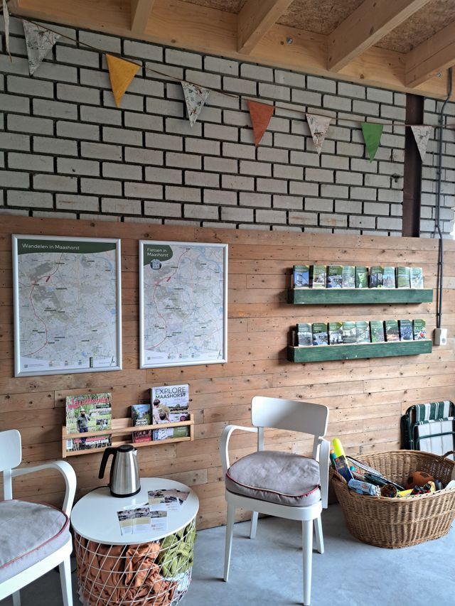 Informatiehoek met stoelen en tafel, wandkaarten ‘Wandelen in Maashorst’ en ‘Fietsen in Maashorst’, en planken met folders en brochures.
