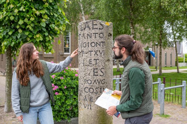 Mensen kijken naar stenen zuil met Romeins geschrift in Valkenburg ZH
