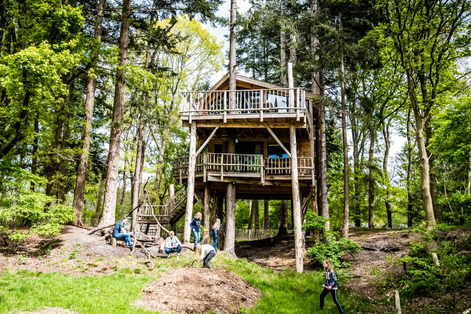 Een gezin vermaakt zich buiten op het gras naast een luxe boomhut.