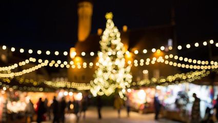 Overzichtsfoto kerstmarkt bij nacht met grote kerstboom in het midden en twinkelende lichtjes rondom.