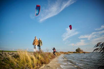 Twee mensen wandelen achter elkaar langs het IJsselmeer bij het Mirnser Klif met kites in de lucht.