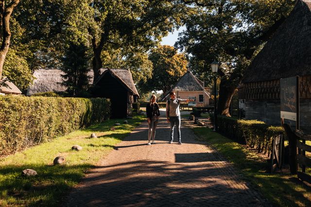 Twee mensen wandelen langs boerderijen door het esdorp Zweeloo en wijzen iets aan.