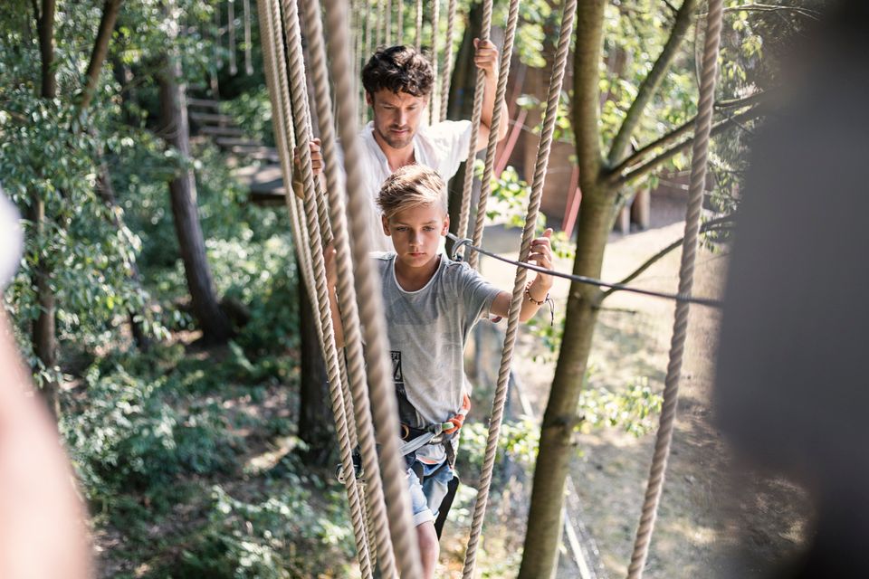 Vader en zoon lopen over een touwbrug in het klimpark.