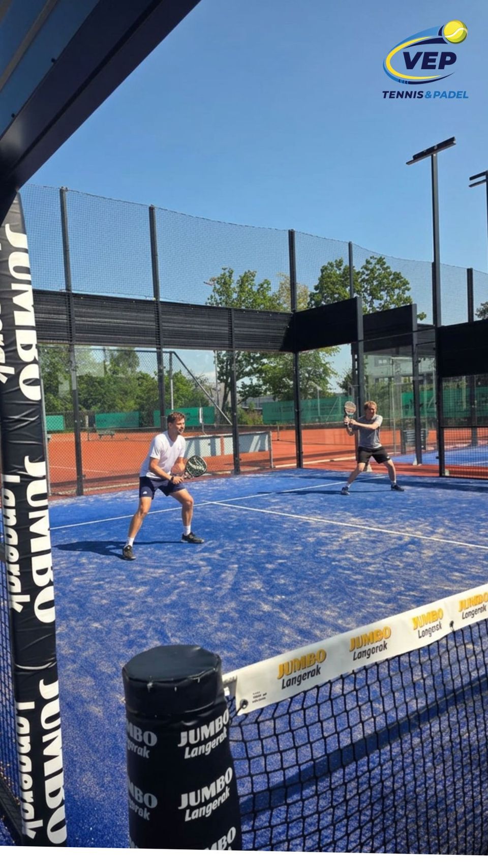 Padelbaan bij VEP Tennis & Padel, met twee spelers tijdens een padelwedstrijd op een blauwe buitenbaan met glazen wanden en sportnetten.