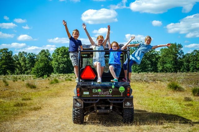 Kinderen staan met hun handen in de lucht in de achterbak van een elektrische terreinauto.