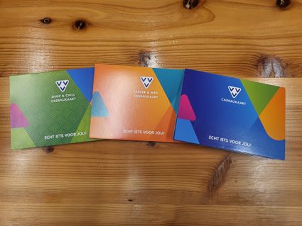 Cadeaukaartenset VVV Cadeaukaarten op houten tafel, diverse thema’s zoals Shop & Chill en Lekker & Weg, Nederland, veelzijdige cadeaubonnen voor winkelen, uitjes en belevenissen.