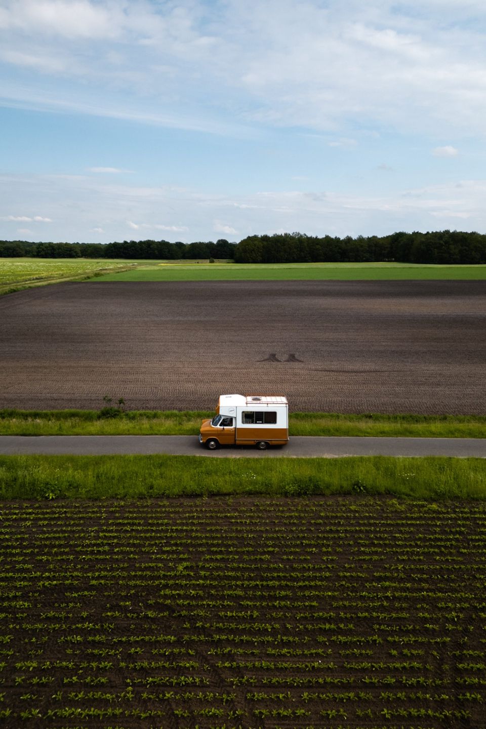 Een kampeerbusje rijdt over een weggetje tussen de akkers in Drenthe.