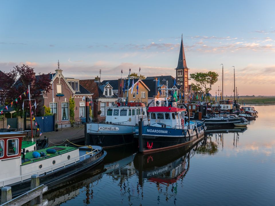 Een stel bewoonde oude sleepboten liggen bij stil water en zonsondergang aan elkaars zij in Woudsend.