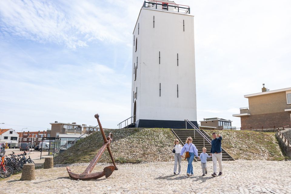 Een gezin loopt voor de witte Vuurbaak in Katwijk aan Zee, de een na oudste vuurtoren van Nederland.