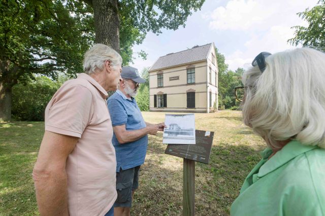 Een man en vrouw zijn op pad met een erfgoedgids. Hij vertelt hen over het monument Ruimzicht. Een statig gebouw in Veenhuizen.