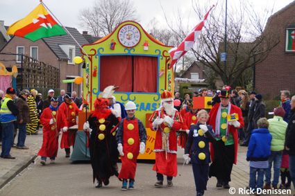 Kleurrijke wagen in de Moergestelse kleuren geel, rood en groen met verklede mensen ervoor en langs de weg.