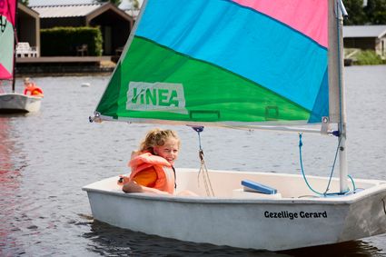 Een lachend meisje zeilend in een optimist met een velgekleurd zeil op het Nannewiid.