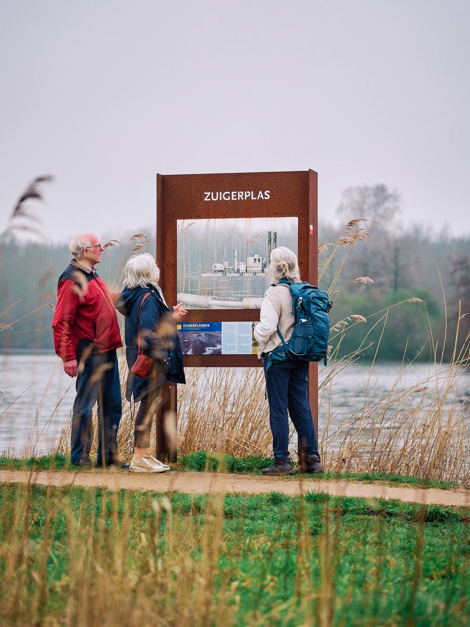 Drie mensen staan tijdens hun wandeling stil bij een doorkijkpaneel