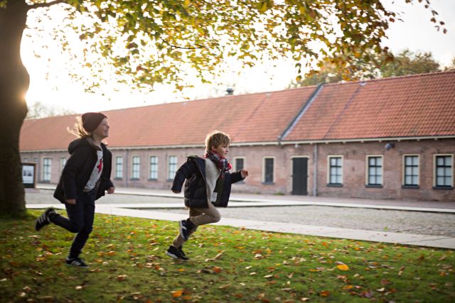 Een jongen en meisje rennen over het binnenterrein van het Gevangenismuseum. Ze hebben het er warm van, want ze rennen met hun jassen open op een niet heel warme dag in november.
