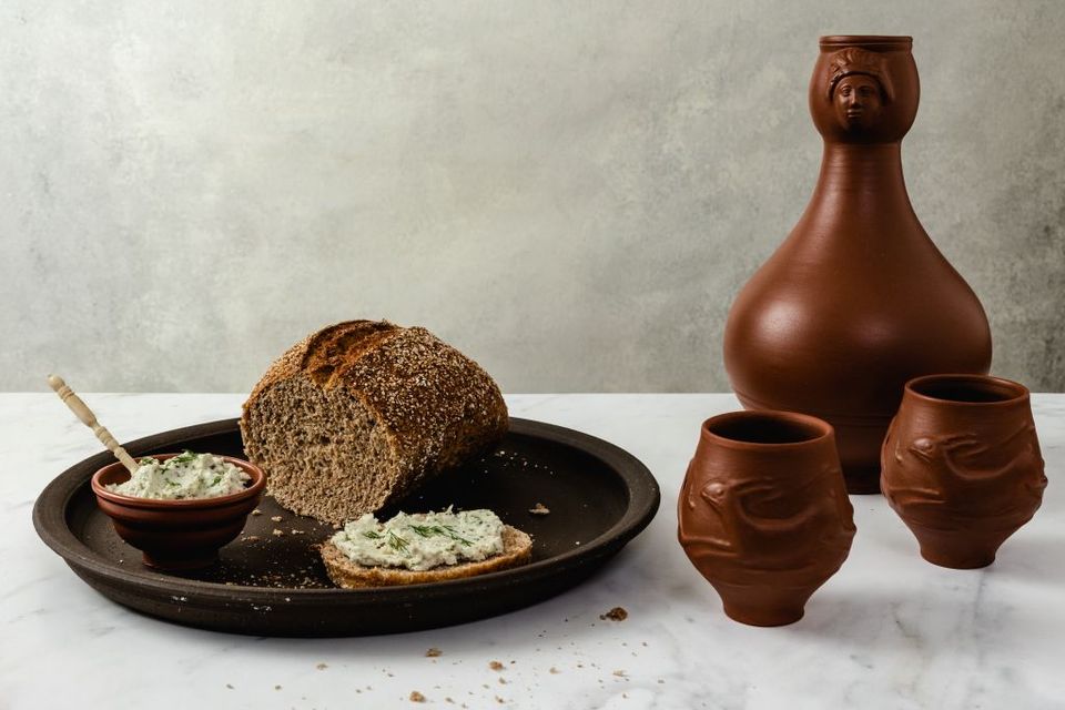 Een kruik, twee kommen en een bord met brood en moretum, een zuivelspread met kruiden.