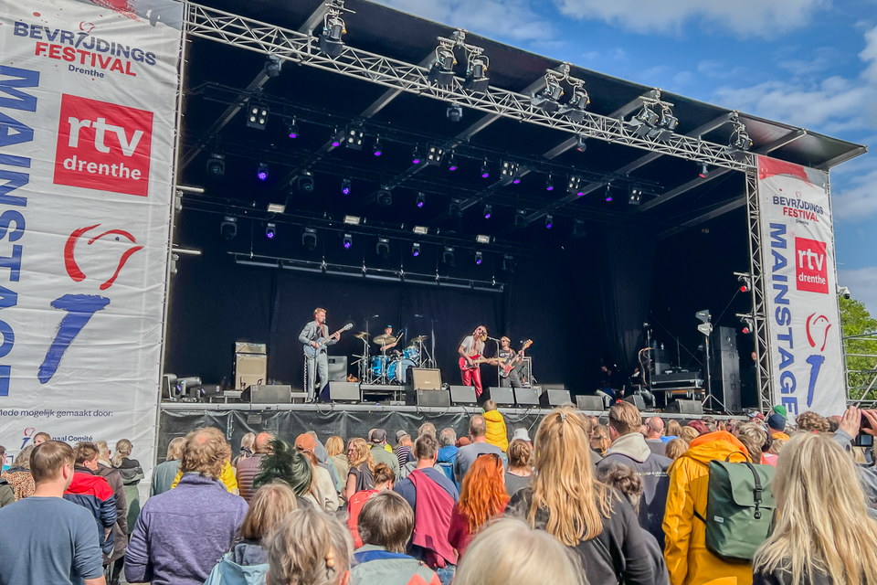 Een menigte mensen staat voor een podium waar iemand optreedt tijdens een festival.