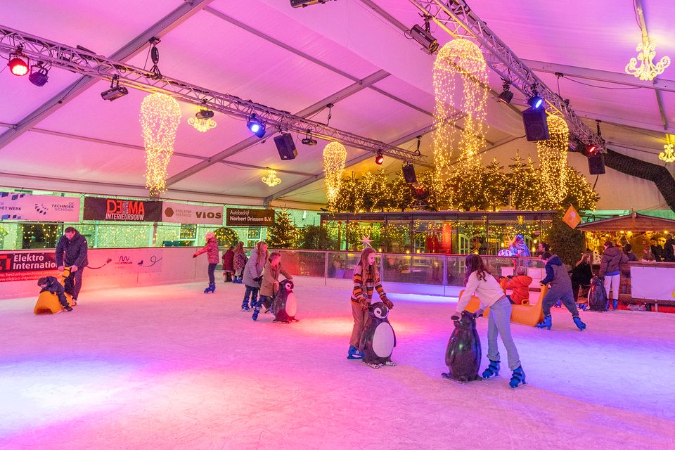 Kinderen schaatsen op de overdekte ijsbaan in Woerden, omringd door warme kerstverlichting en winterdecoratie; een sfeervolle winteractiviteit in het Groene Hart die uitnodigt tot gezelligheid en winters plezier.