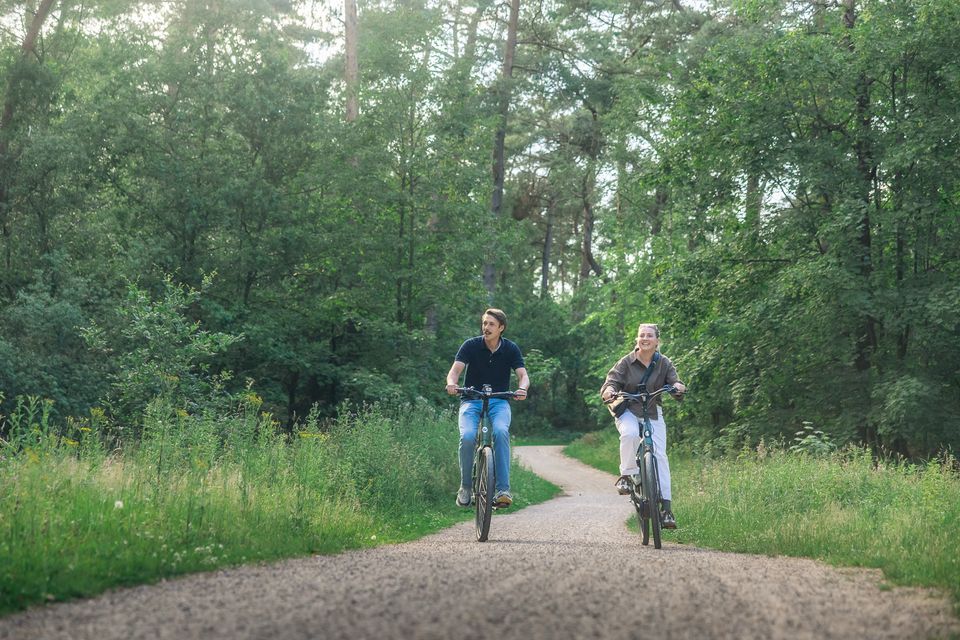 Een man en een vrouw op een fiets over een grindpad in het bos.