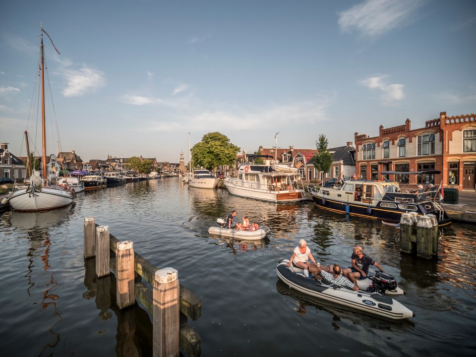 Een gracht in lemmer waar allemaal boten aan de zijkant staan, ook varen er twee speedboten.