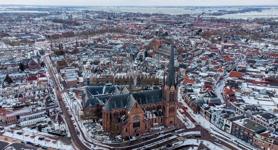 Een indrukwekkende luchtfoto van Woerden onder een frisse sneeuwdeken. De imposante kerk vormt het stralende middelpunt van het historische centrum, terwijl de kronkelende straten en besneeuwde daken de stad een bijna sprookjesachtige winteruitstraling geven. Een prachtig overzicht van Woerden in haar meest serene seizoen.