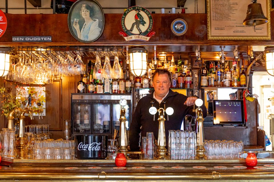 Café de Pompier in Woerden, regio Groene Hart, horecalocatie met terras en glazen pui voorzien van rode banner en slogan, vastgelegd tijdens de 40-jaar-reünie bij deze bekende uitgaansgelegenheid in het centrum.