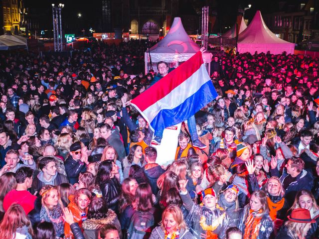 Veel mensen bij Oranjekoorts met een man die een Nederlandse vlag vasthoud op het Marktplein in Delft
