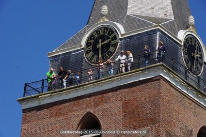 Historische kerktoren Petrustoren in Woerden, Groene Hart, met bezoekers op de omloop bij de grote wijzerplaten tijdens een torenbeklimming met uitzicht over de vestingstad en het Utrechtse landschap.