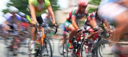 Wielerwedstrijd Ronde van Woerden, Groene Hart, dynamisch peloton van wielrenners in kleurrijke tenues dat met hoge snelheid door het centrum raast, vastgelegd met bewegingsonscherpte tijdens een sportief evenement.